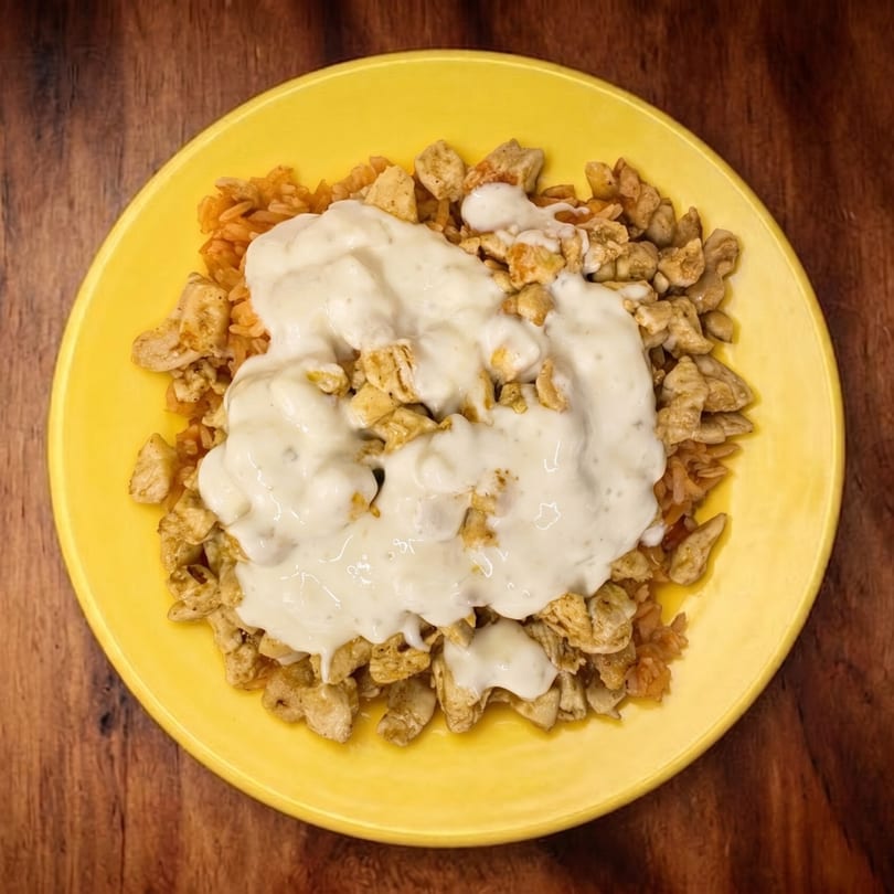Overhead view of a yellow plate with chicken and rice, topped with a creamy white sauce.