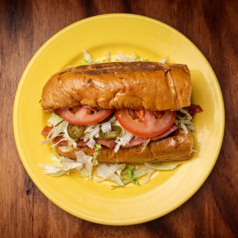 A toasted sub sandwich with tomatoes, jalapeños, and shredded lettuce on a yellow plate.
