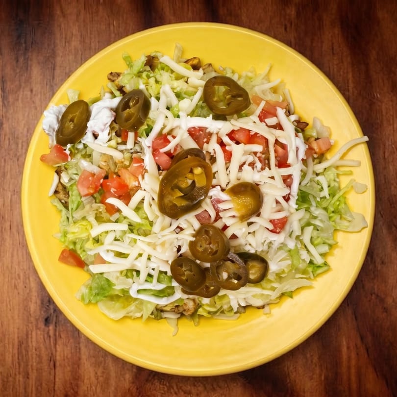 A yellow plate of nachos with lettuce, tomatoes, shredded cheese, sour cream, and jalapeños.
